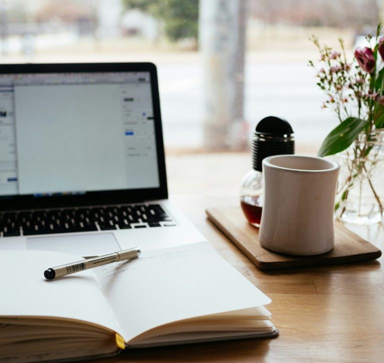 Ein Laptop mit geöffneter Webseite auf einem Tisch, umgeben von einer Tasse und einem Smartphone.